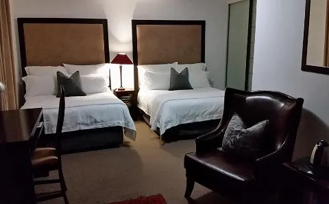 Two neatly made beds in a dimly lit bedroom with a leather armchair