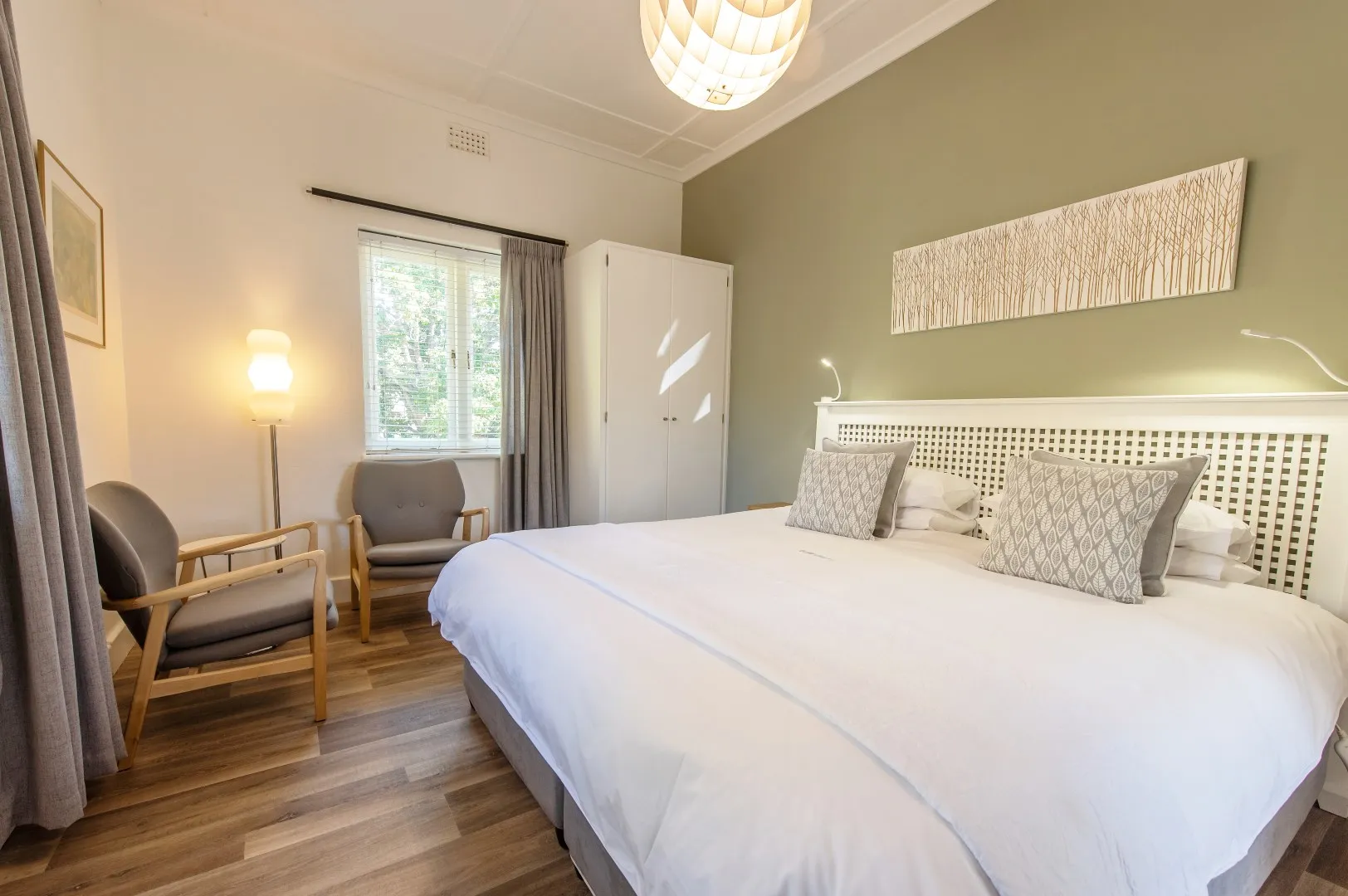 Modern bedroom with white bed green wall wooden chairs and large window