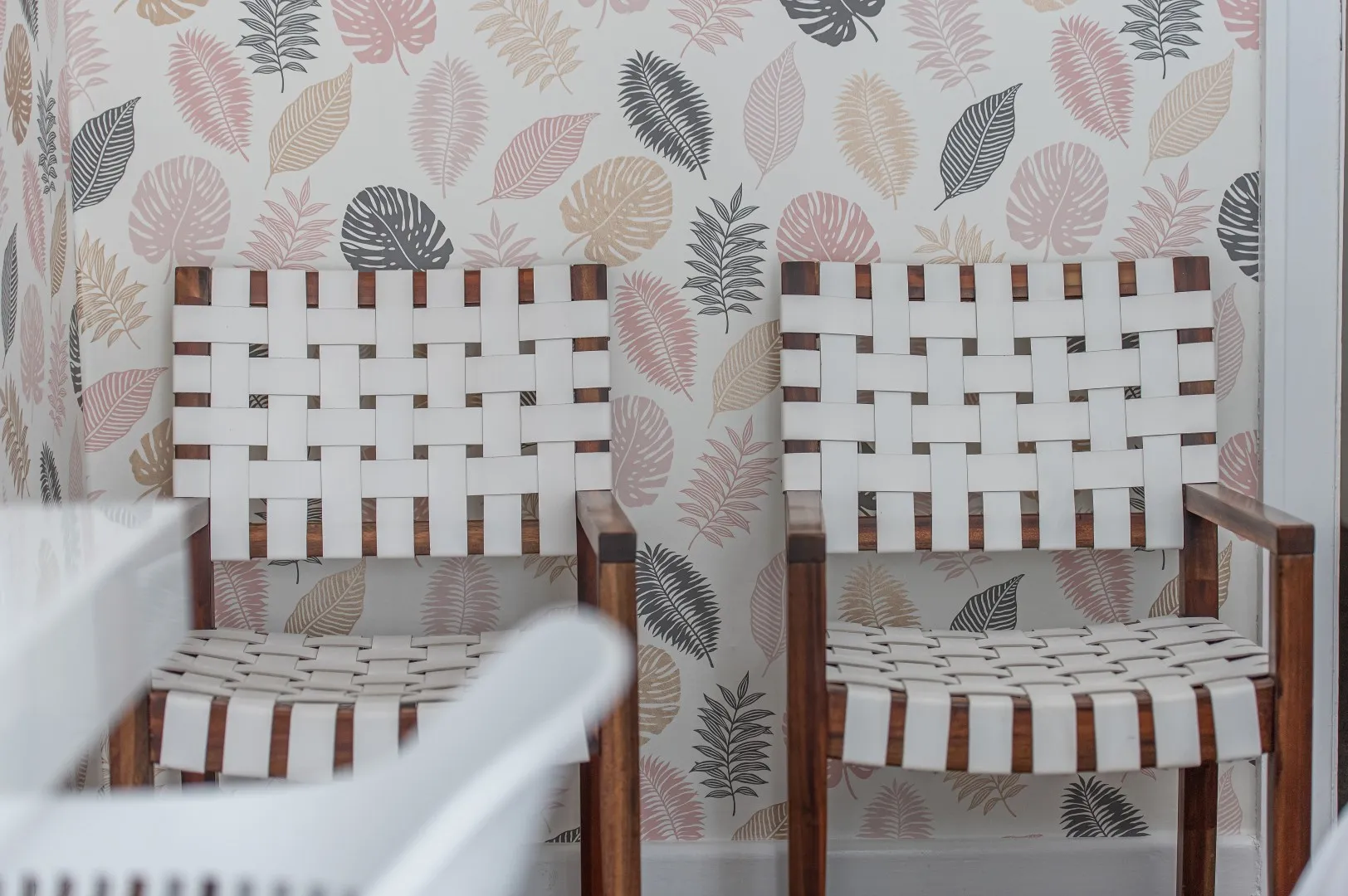 Two white woven chairs in front of a floralpatterned wall