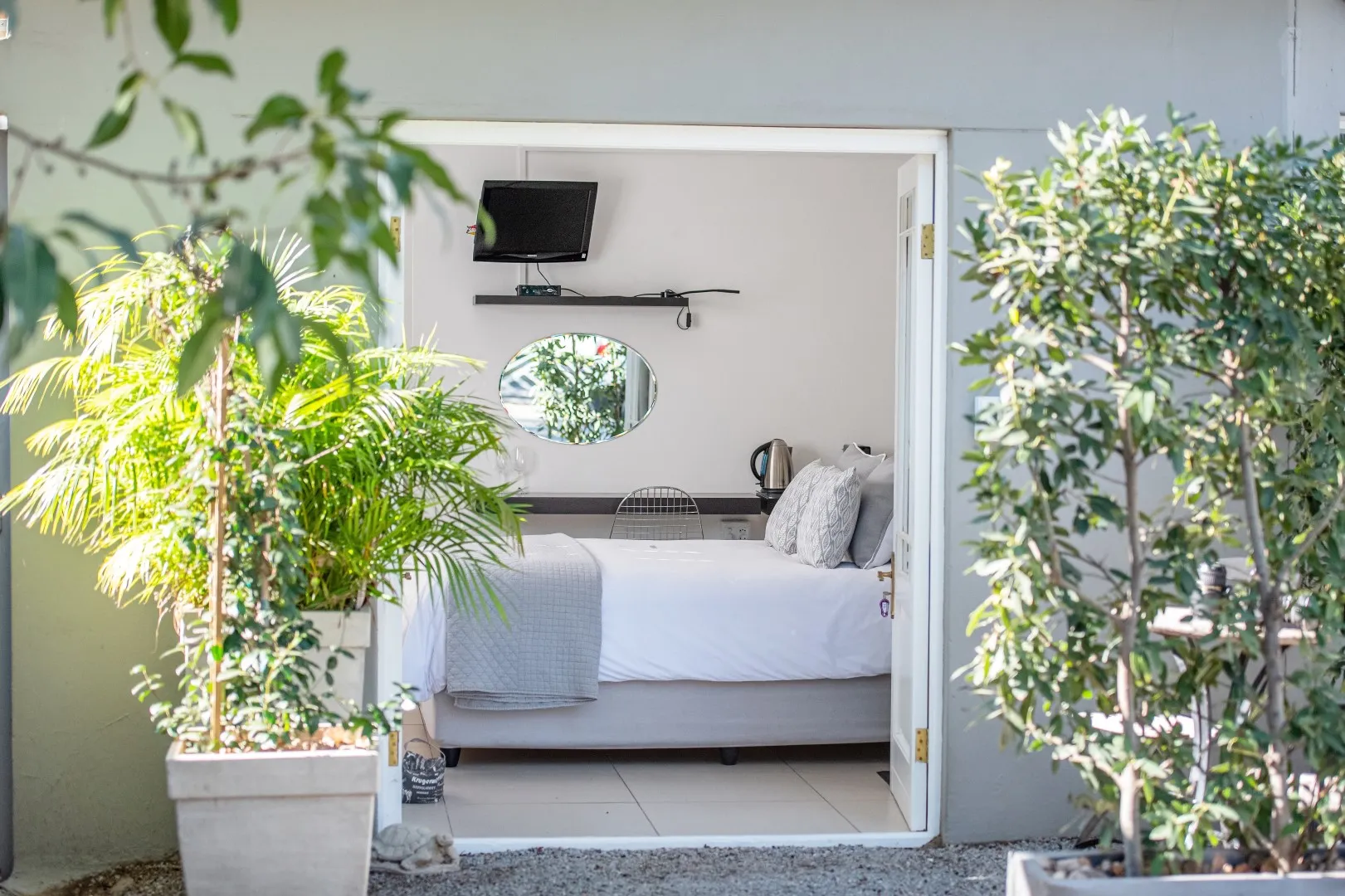 Bedroom with open door plants outside bed with pillows and a TV mounted above