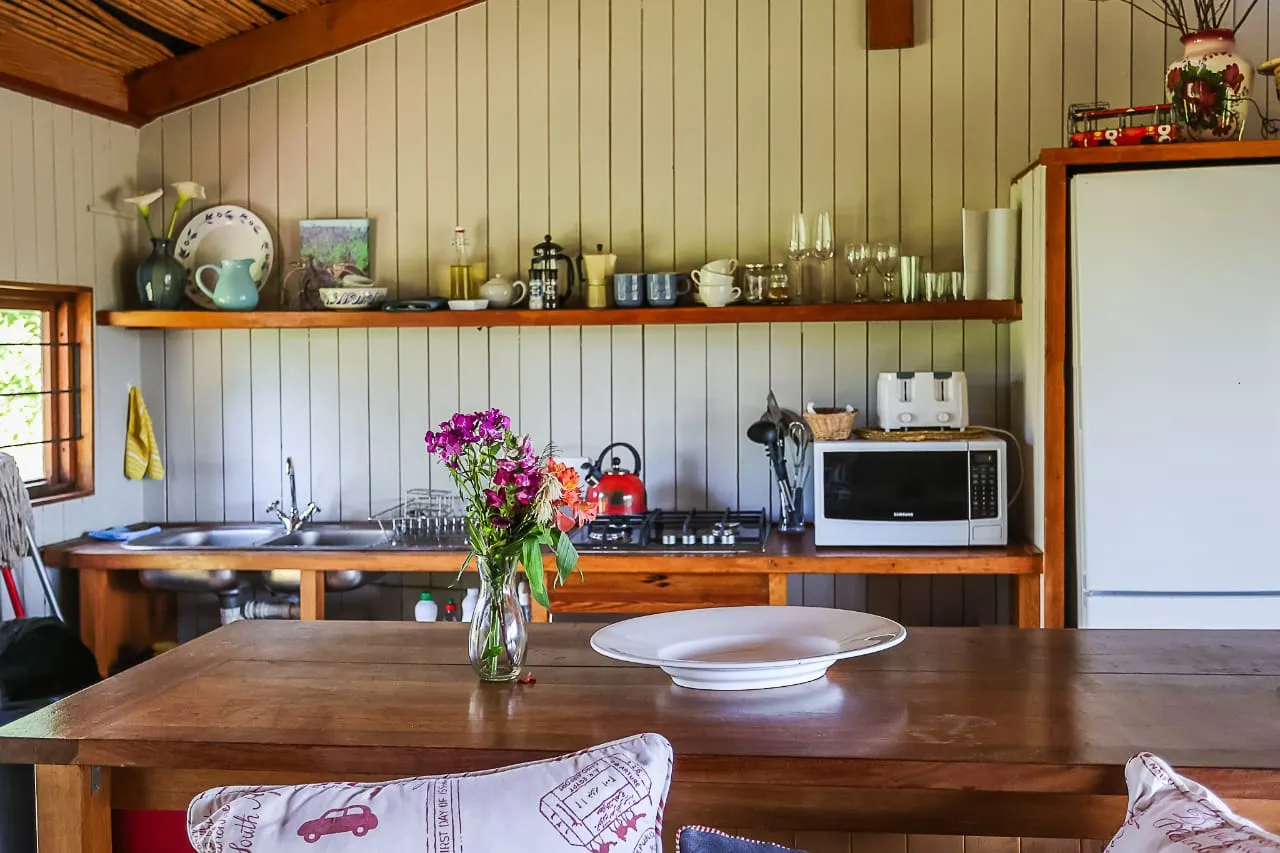 Wooden kitchen with shelves sink microwave and a vase of flowers on table