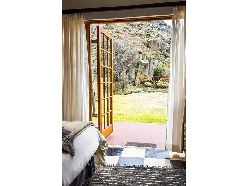 Open door to garden view from a bedroom with a bed and curtains