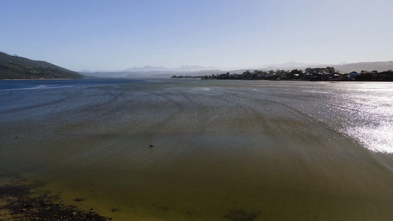 Coastal landscape with calm water distant hills and buildings under a clear sky