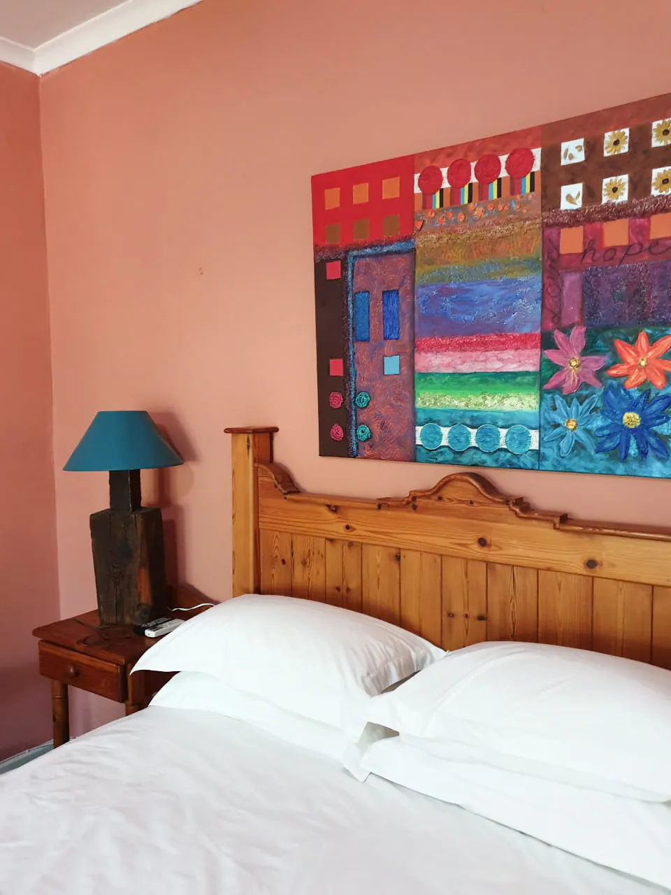Wooden bed with white linens and colorful abstract painting on peach wall