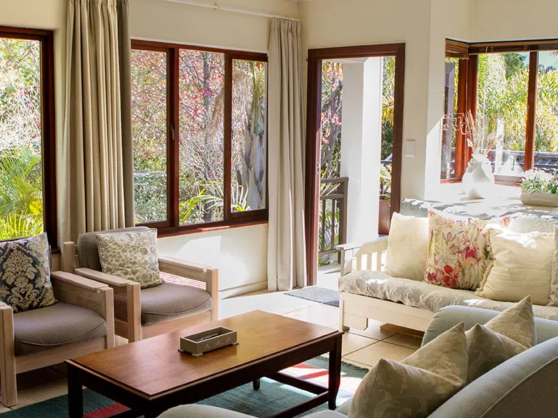 Sunlit living room with sofas chairs and large windows overlooking a garden