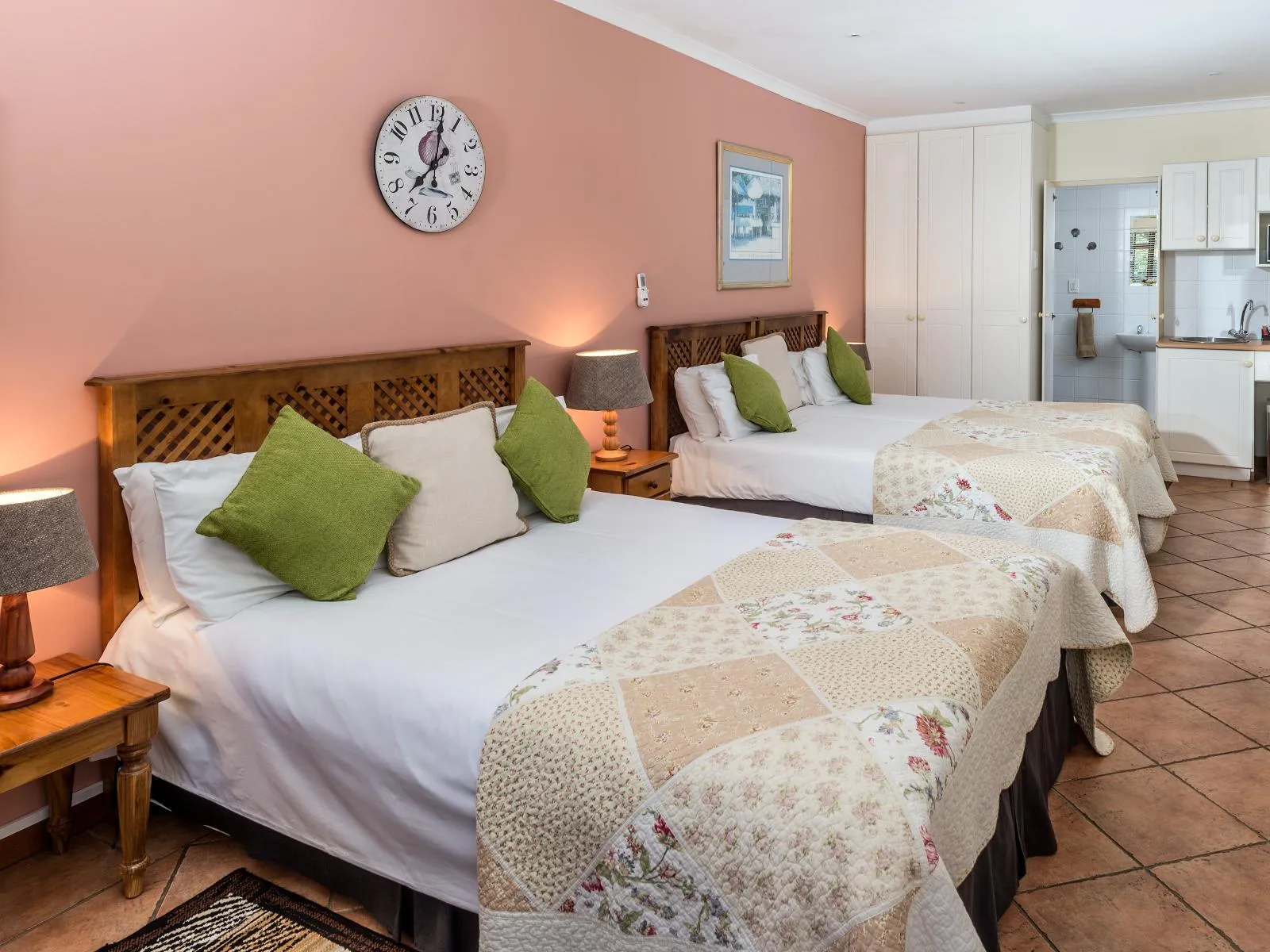 Two neatly made beds in a cozy peachcolored bedroom with a clock on the wall