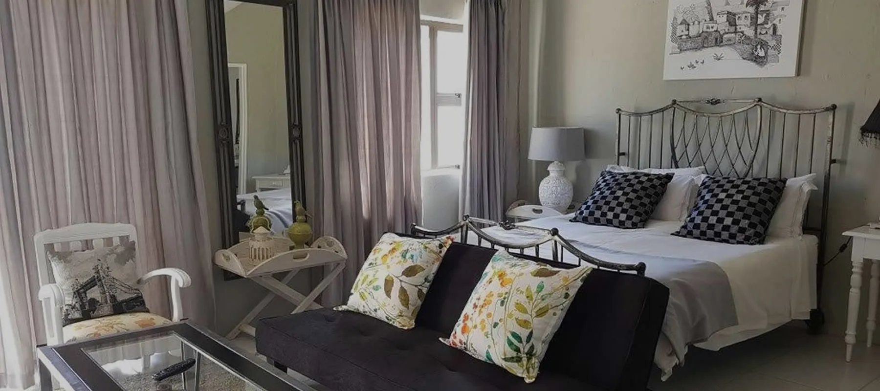 Bedroom with a bed couch and decorative pillows featuring striped curtains and artwork