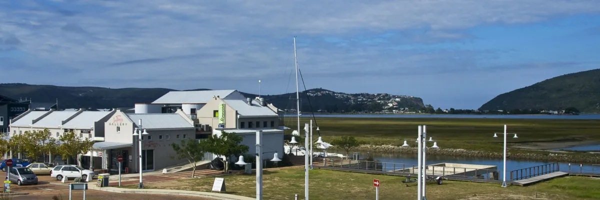 Modern buildings near a waterfront with boats and hills in the background