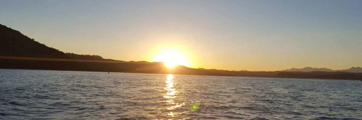 Sunset over a calm sea with distant mountains and a clear sky
