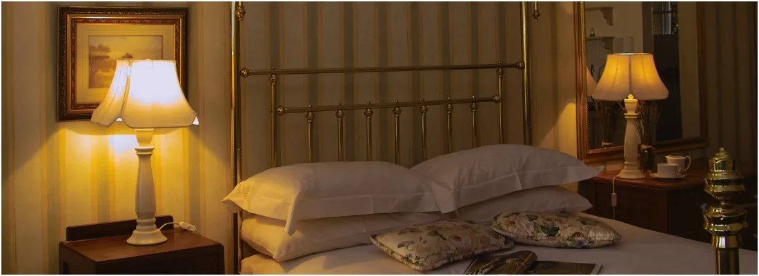 A cozy bedroom with a bed lamps and pillows warmly lit at night