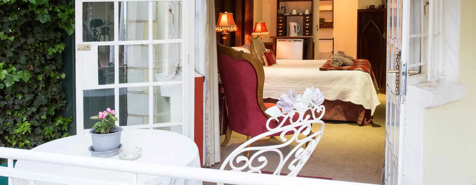 Balcony with white table and chairs overlooking a cozy bedroom with a bed