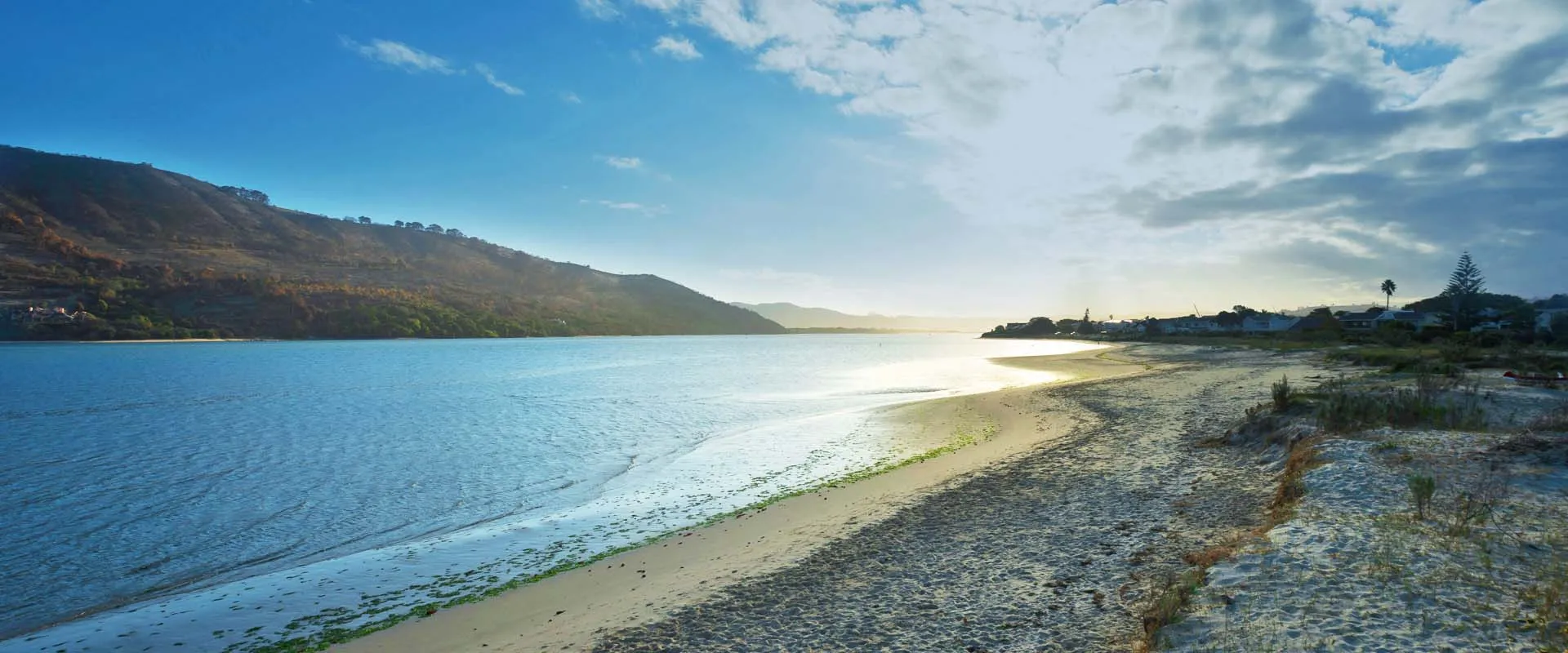 Beach with clear blue water mountains in the background and a partly cloudy sky