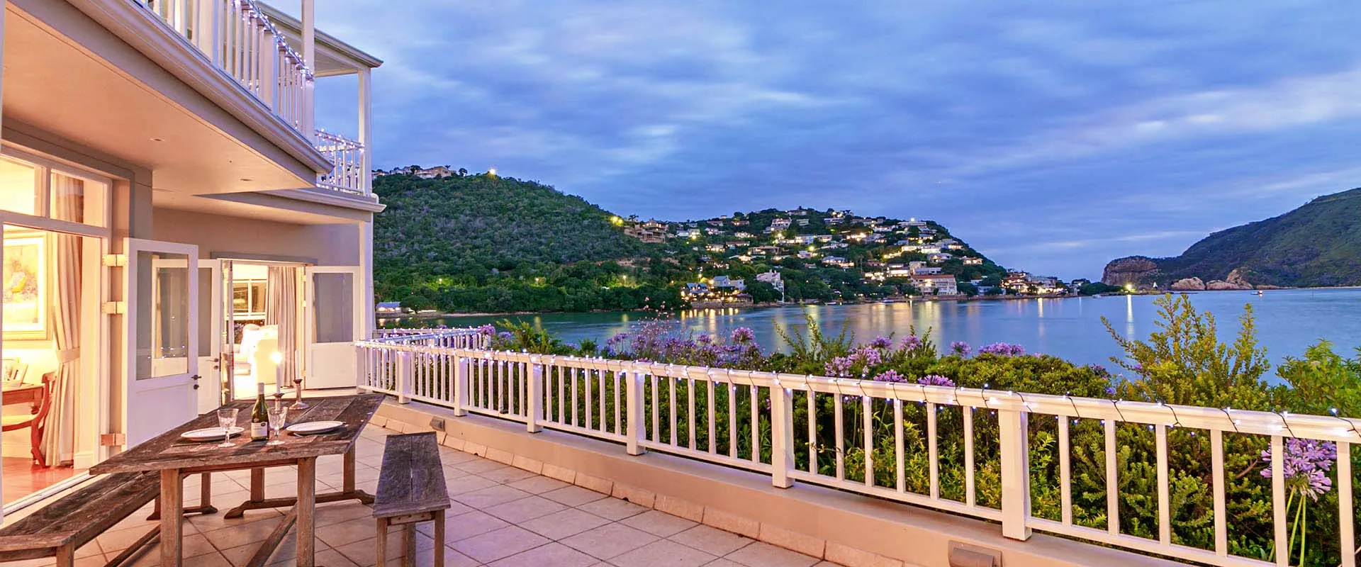 House with outdoor seating overlooking a lake and hills at dusk