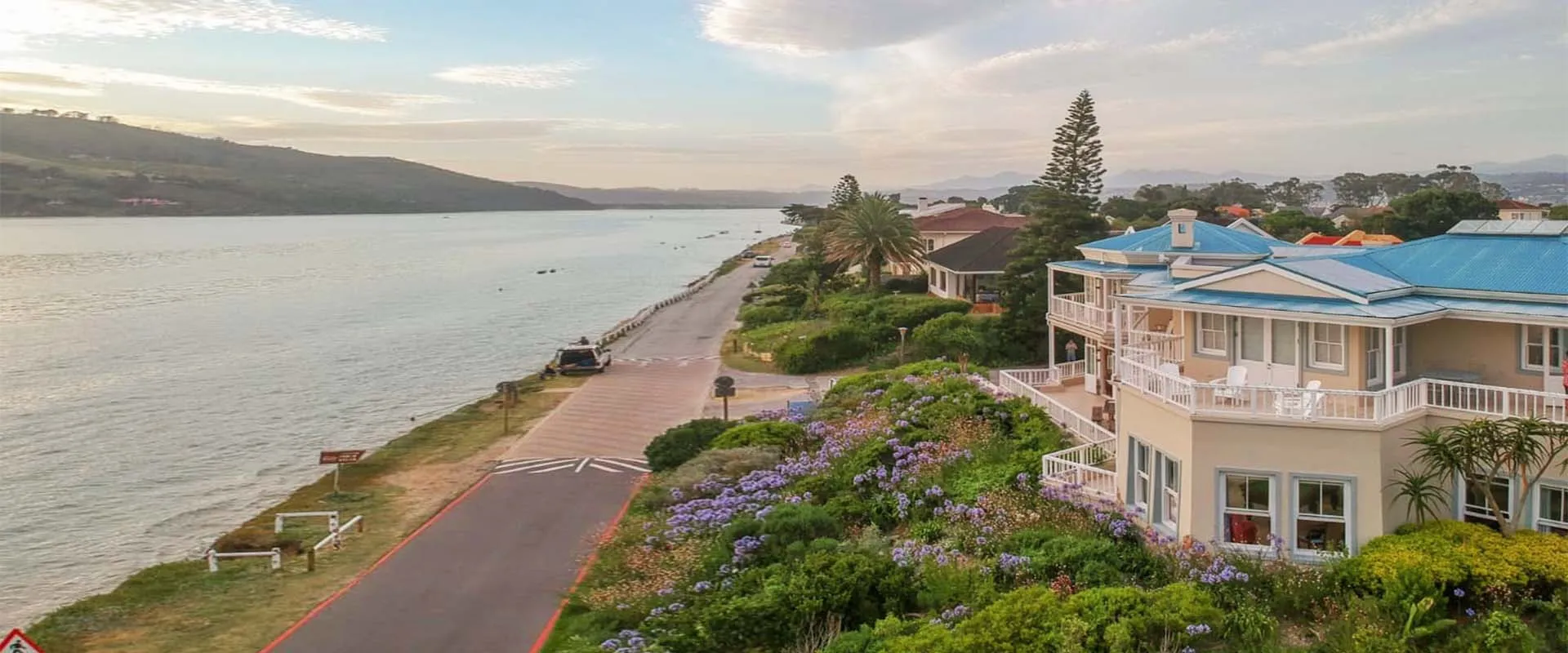 Houses along a waterfront with a road and lush greenery