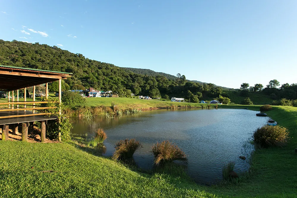 Wooden deck overlooking a serene pond in a lush green hilly landscape