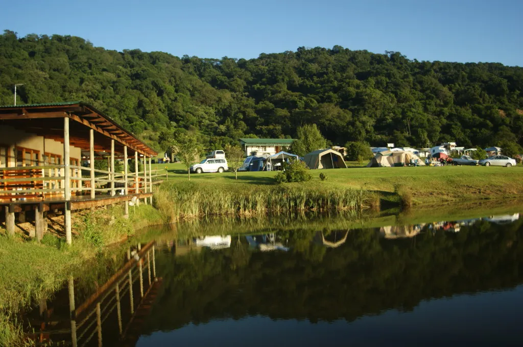 Campsite with tents and cabins by a lake surrounded by lush green hills