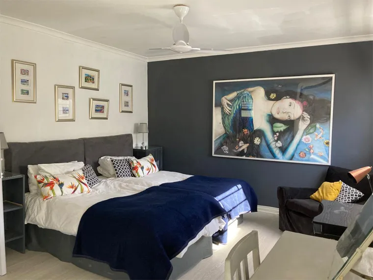Bedroom with large bed dark blue blanket and a large painting on the wall