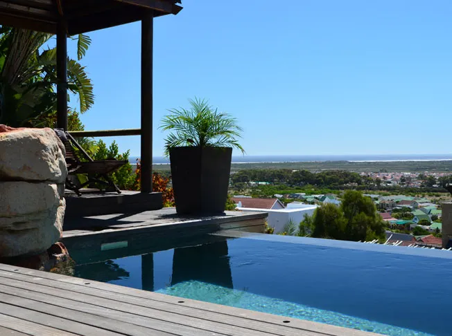 Infinity pool with potted plant overlooking a scenic town and blue sky