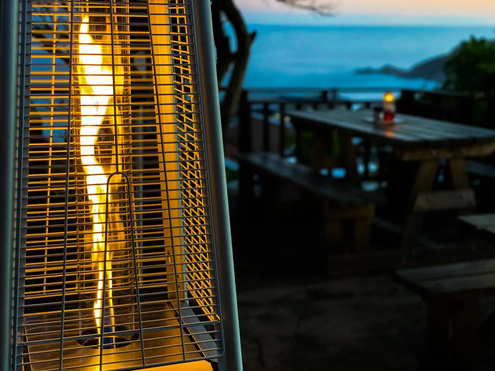 Outdoor patio with a lit heater picnic tables and ocean view at dusk