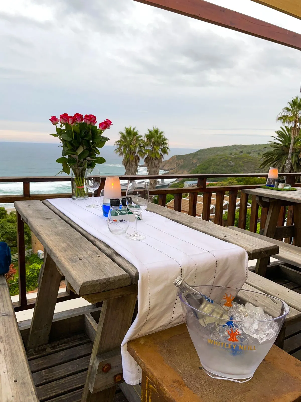 Wooden table with white runner wine glasses and ocean view from a deck