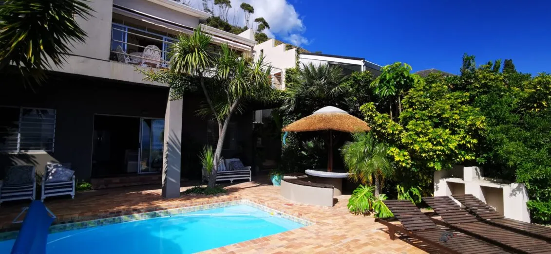 Modern house with pool lounge chairs and lush greenery under a clear sky