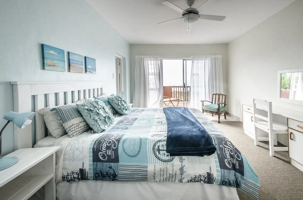 Bedroom with nauticalthemed bedding ceiling fan and large window with curtains