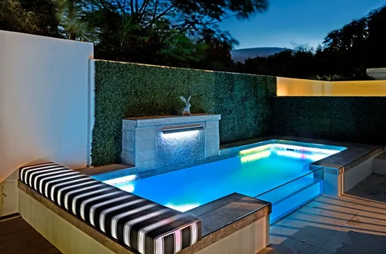 Modern pool with underwater lighting surrounded by greenery and a seating area