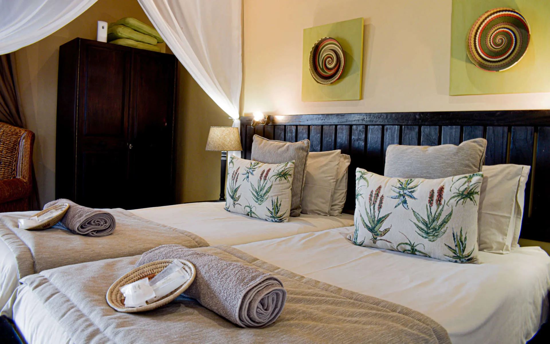Two beds with floral pillows rolled towels and decorative wall art in a bedroom