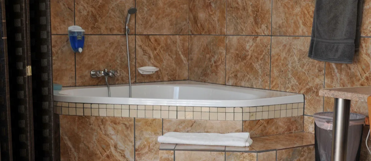 Corner bathtub in a tiled bathroom with towels and a soap dispenser