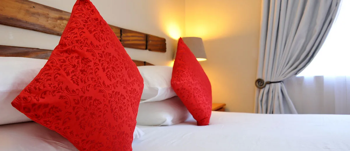 Red pillows on a bed with a lamp in the background