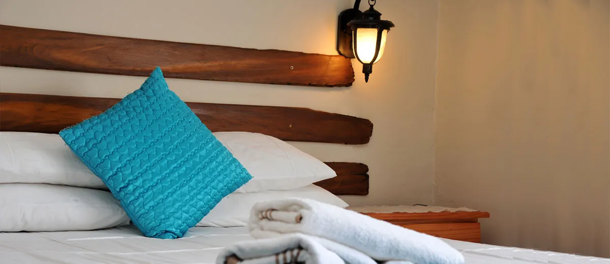 Bed with turquoise pillow white linens and wooden headboard in cozy room