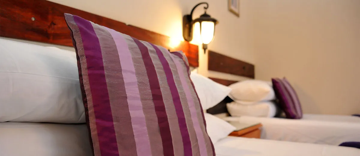 Closeup of purple striped pillows on a bed in a bedroom with wall lamp