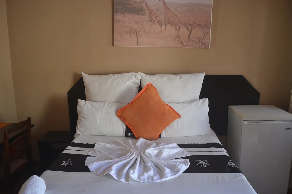Neatly made bed with white towels and orange pillow in a simple room