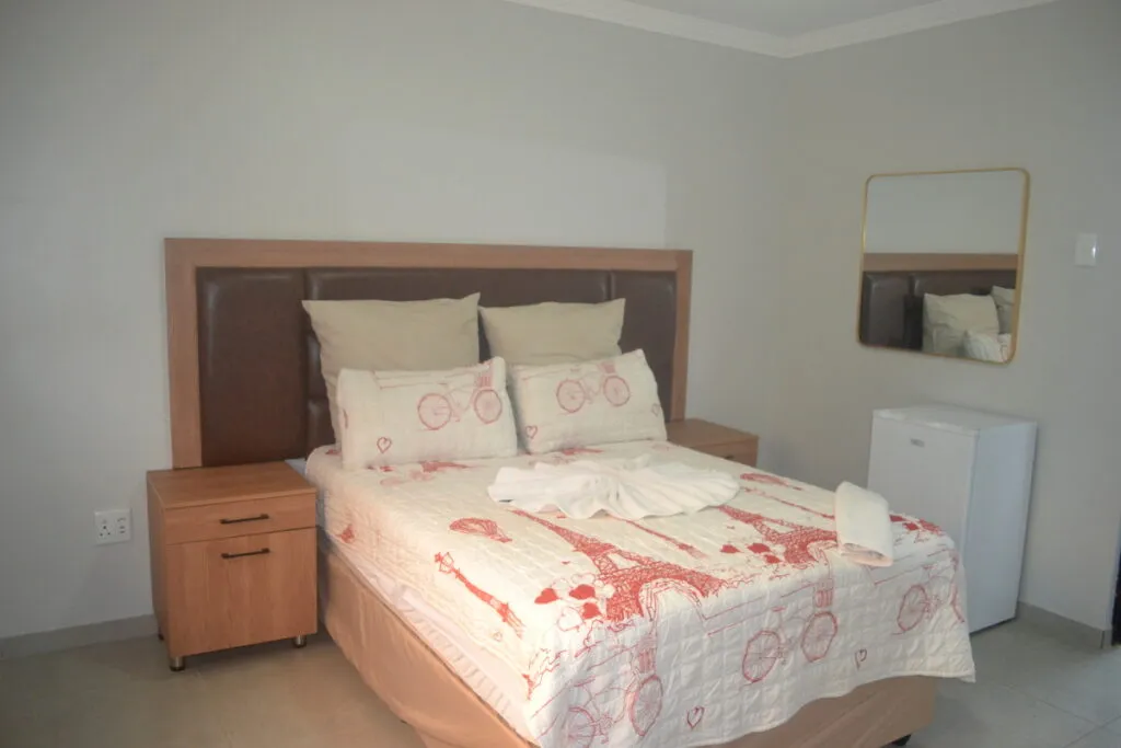 Bedroom with double bed wooden headboard bedside table mirror and small fridge