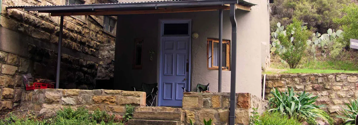 Stone house with a blue door covered porch and surrounding greenery