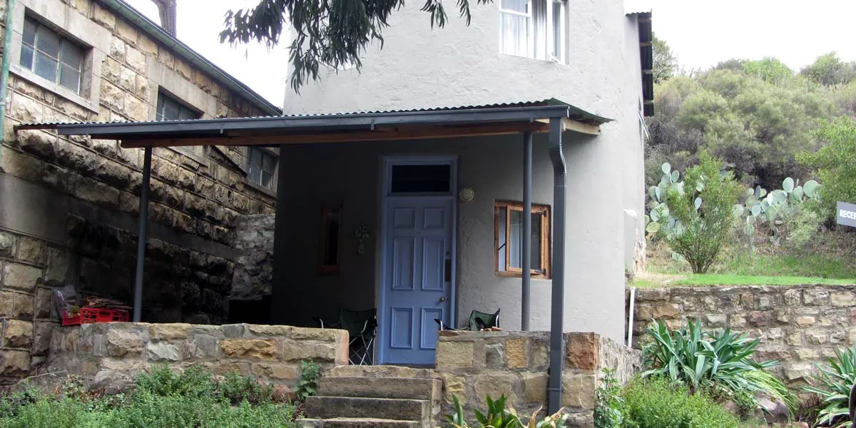 Small stone house with blue door and covered porch surrounded by greenery