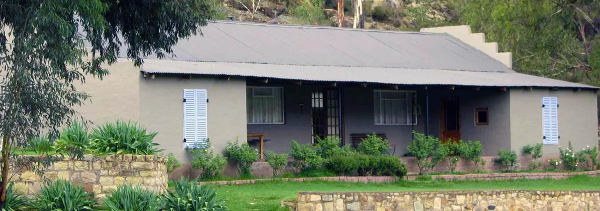 Singlestory house with a grey roof surrounded by greenery and stone walls