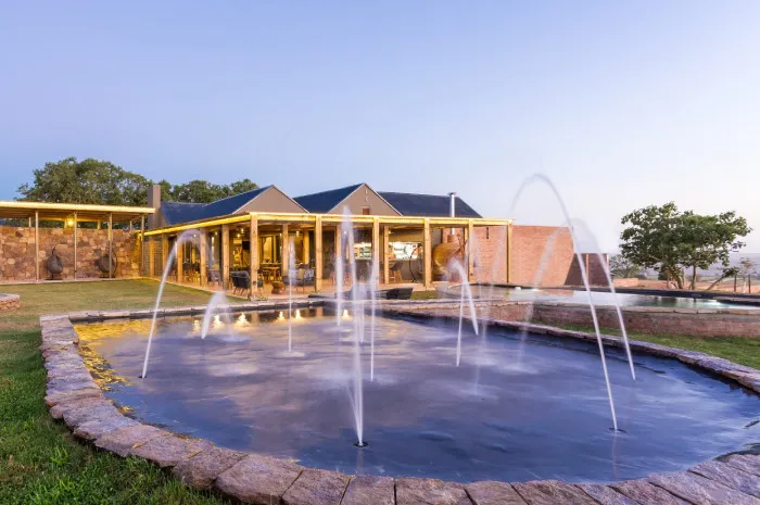 Water fountain in front of a modern house with a pool at sunset