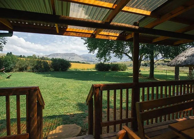 Wooden deck overlooking green field with trees and distant mountains under a blue sky