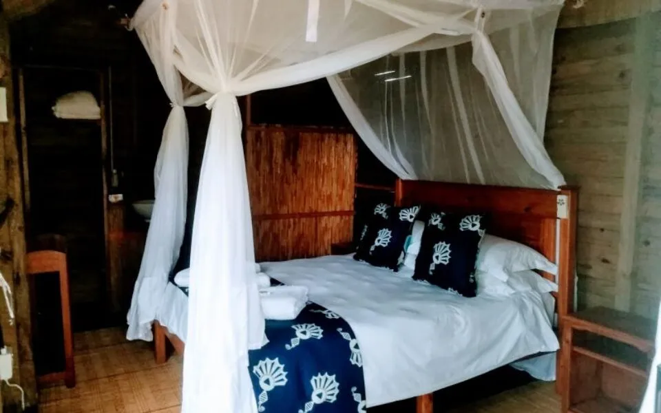 Wooden cabin bedroom with a bed under a mosquito net and nauticalthemed bedding