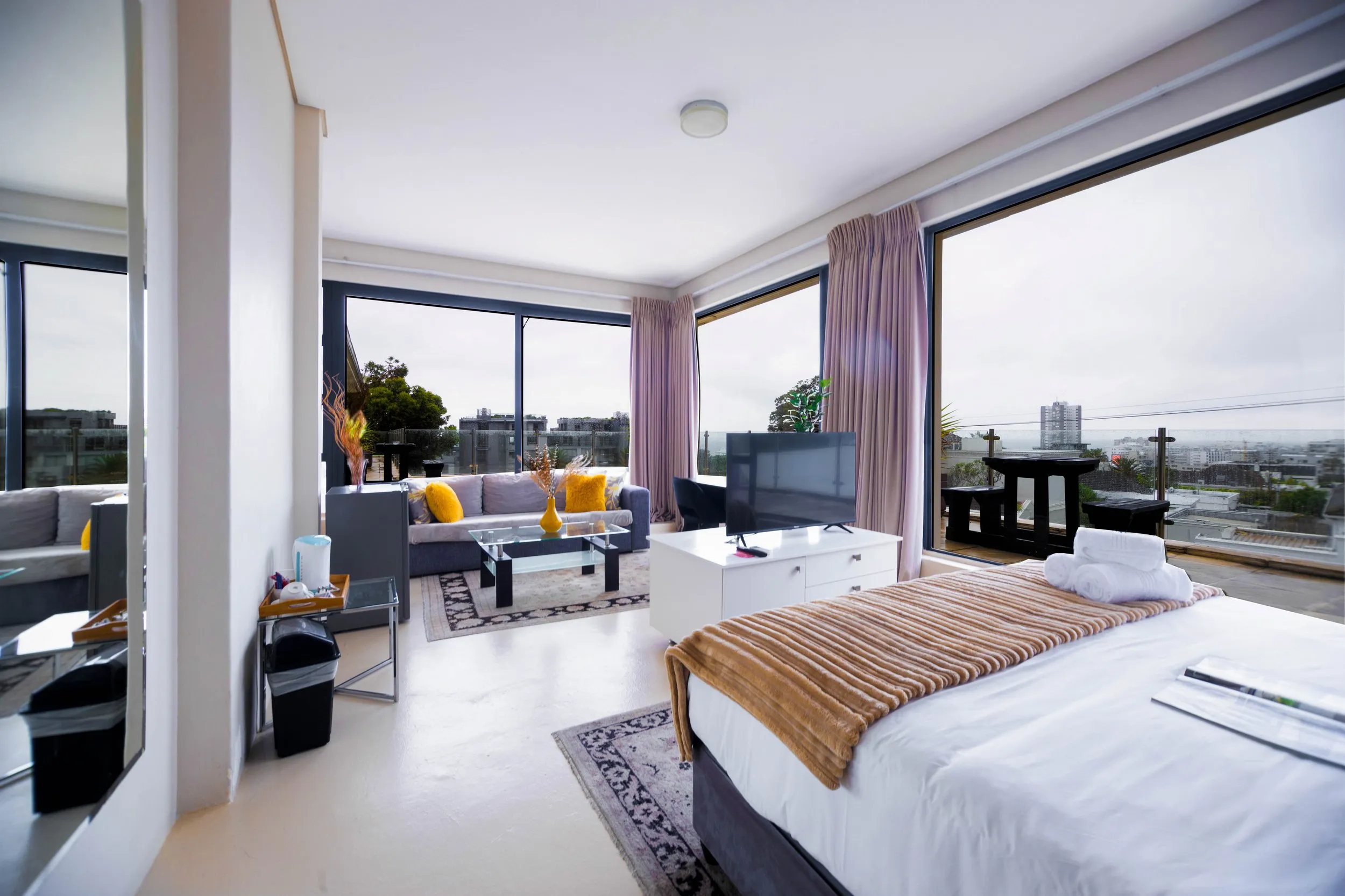 Modern hotel room with large windows bed sofa and city view