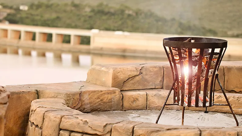 Fire pit with flames on stone patio overlooking a serene water body