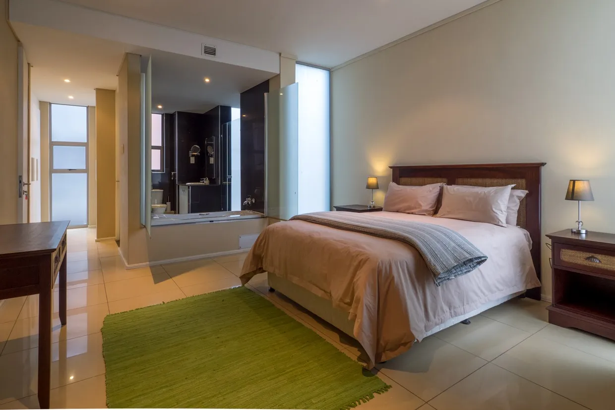 Modern bedroom with large bed green rug and attached bathroom visible through mirror