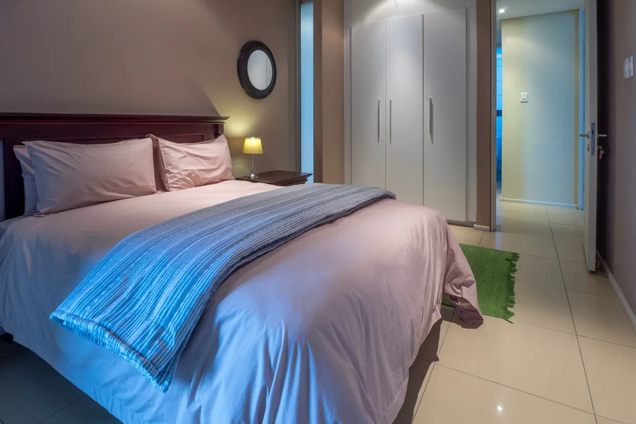 Bedroom with a neatly made bed bedside lamp and open door to another room