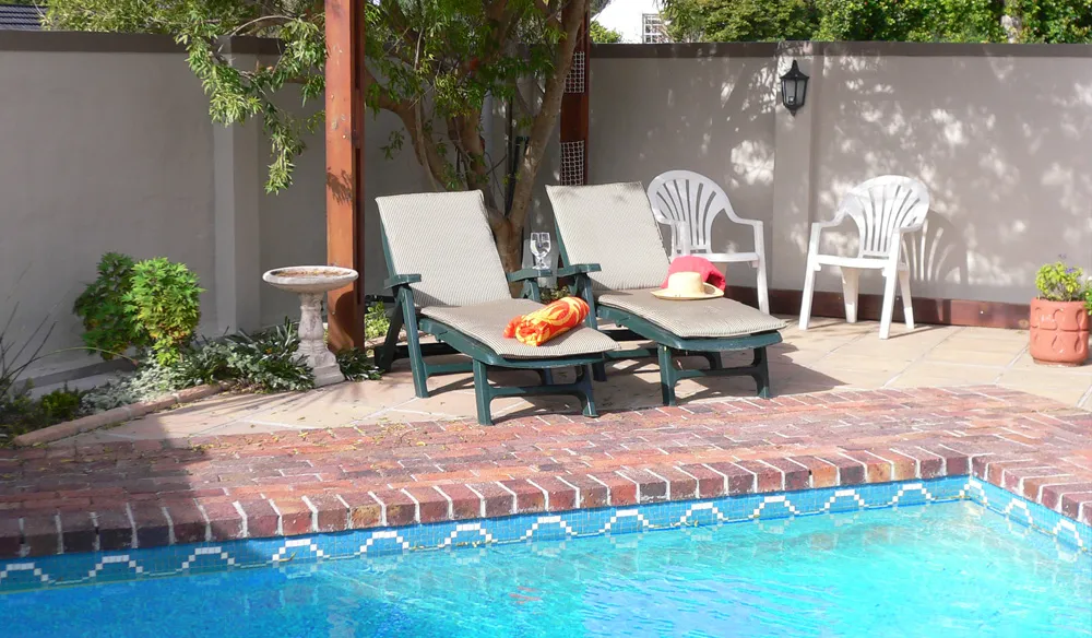 Two lounge chairs by a pool with a potted plant and birdbath nearby