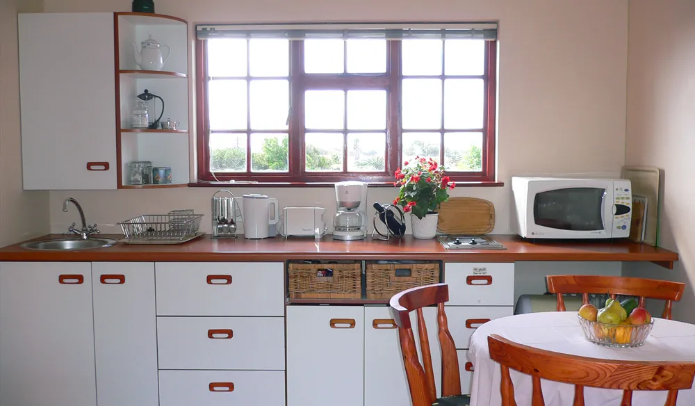 Kitchen with white cabinets microwave sink and a dining table with fruit