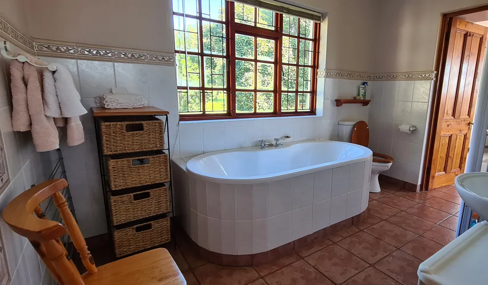 Bathroom with white bathtub toilet wooden chair and large window with view