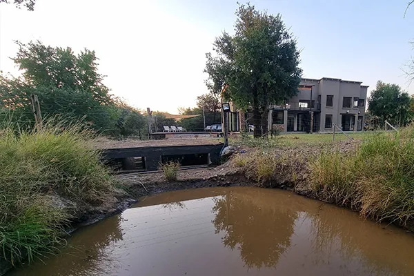 Modern house with a bridge over a muddy pond and surrounding greenery