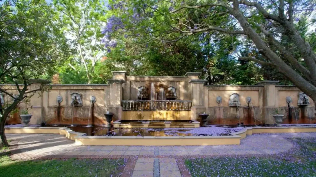 Ornate stone fountain in a lush garden with trees and flowers