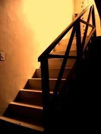 Staircase with wooden railing lit from above in a dimly lit room